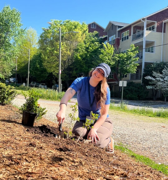 A woman kneeling while gardening and smiling at the camera
