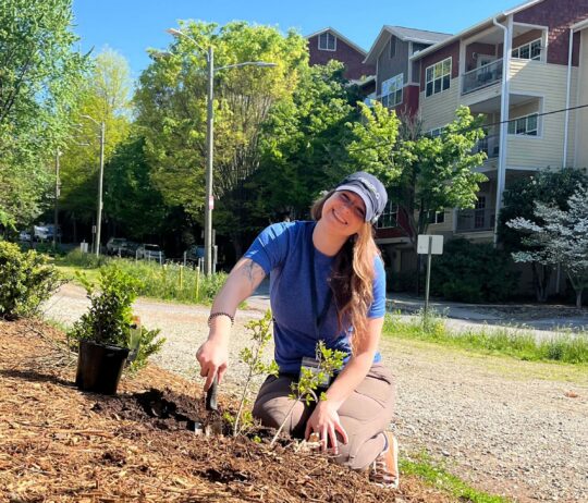 A woman kneeling while gardening and smiling at the camera