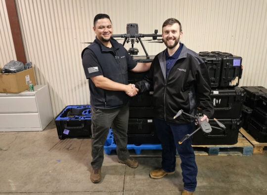 Two men shake hands in front of a drone